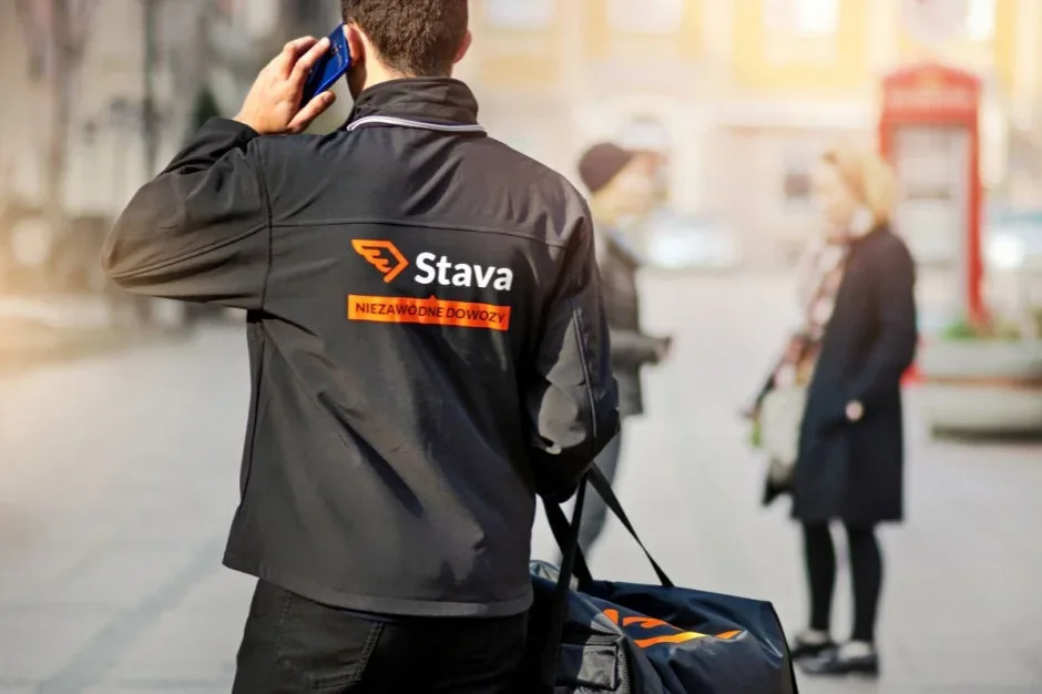 Kurier Stava z torbą dostawczą rozmawia przez telefon na ulicy